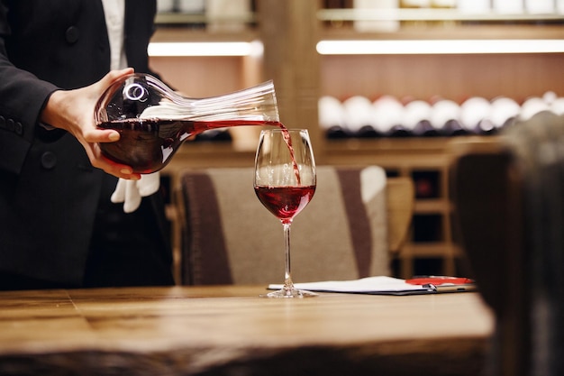 Foto vrouwelijke barman in strenge klassieke kleren die rode wijn uit een drankje naar het glas giet