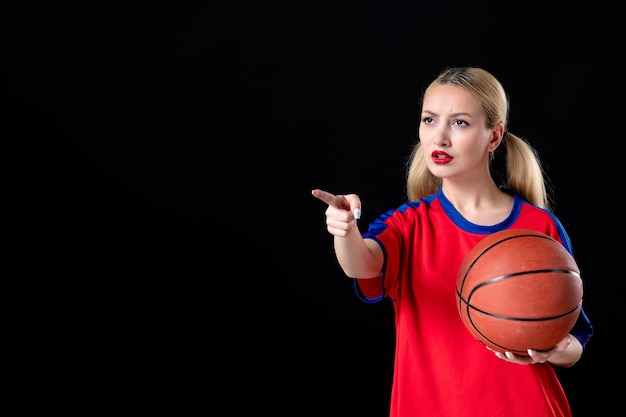 vrouwelijke basketbalspeler met bal wijzend op iets op zwarte achtergrond game atleet play