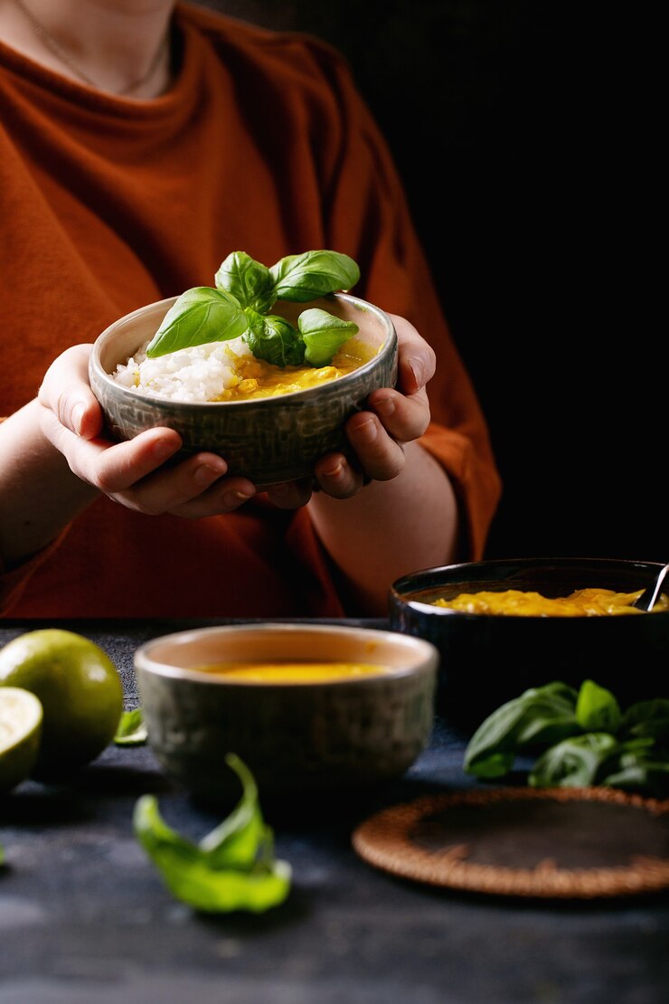 Vrouwelijke bedrijf keramische kom gele curry geserveerd met basilicum en limoenen