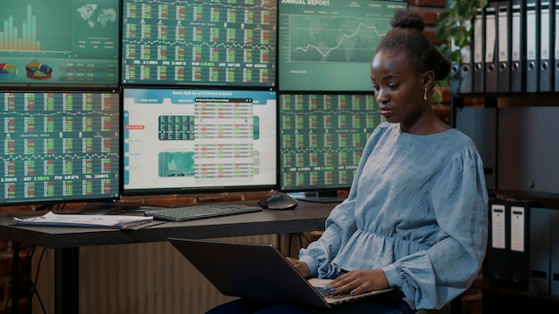 Vrouwelijke belegger kijkt naar realtime aandelen op laptop en meerdere monitoren, analyseert marktkoers en winst. Investeringsaandeel met financiële handelsstatistieken voor hedgefonds.