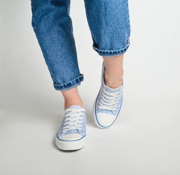 Vrouwelijke benen in korte jeans en sneakers staan op een wit