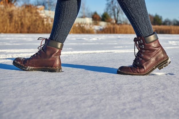 Vrouwelijke benen in leren bruine waterdichte laarzen wandelen in de winter op verse sneeuw. Casual mode, trendy schoenen.