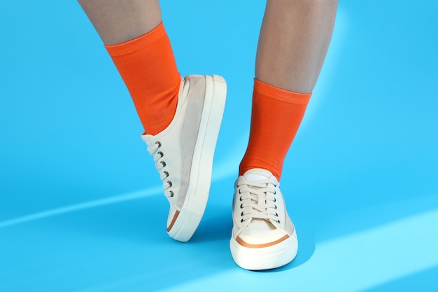 Vrouwelijke benen in oranje sokken en sneakers op blauwe achtergrond