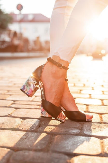 Vrouwelijke benen in witte mode-jeans in elegante leren sandalen staan in de stad bij zonsondergang. Close-up