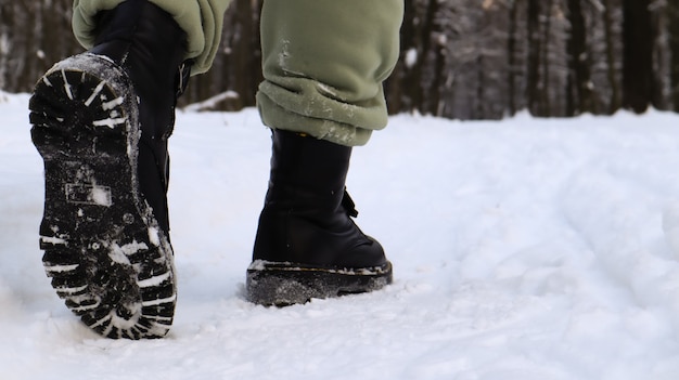 Vrouwelijke benen in zwarte laarzen, winterwandeling in de sneeuw. Actieve vrouw die wegloopt van de camera in het winterbos. Concentreer je op je benen. Mooi wit winterweer met verse sneeuwval.