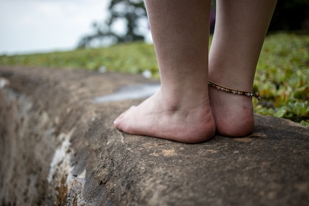 Vrouwelijke benen met een armband aan de kant van de vijver tegen de achtergrond van een natuurlijk landschap