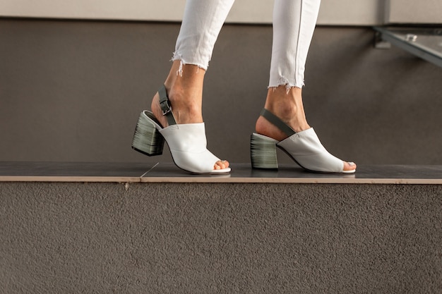 Vrouwelijke benen met mode zomer witte schoenen lopen in de buurt van grijze muur