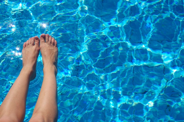 Vrouwelijke benen op de achtergrond van het zwembad Open ruimte juiste watertextuur met zonlichtreflecties