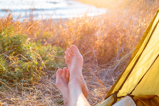 Vrouwelijke benen peek uit een toeristische tent bij zonsopgang aan de kust Reizen en recreatie in de open lucht