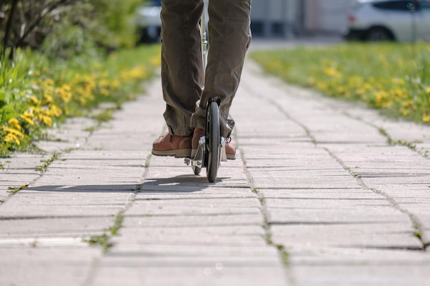 Vrouwelijke benen rijden op een scooter over het trottoir tussen bloeiende gazons