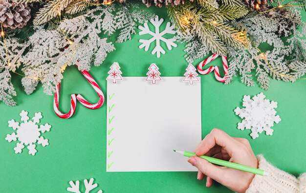Vrouwelijke blanke hand met een pen boven een blanco vel papier met wasknijpers kerstboom