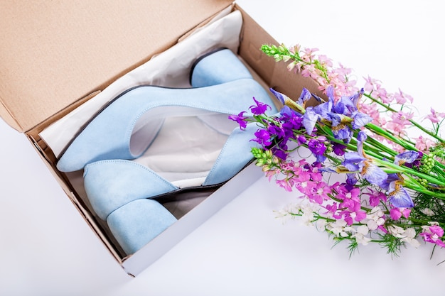 Vrouwelijke blauwe huwelijksschoenen in doos met bloemen op wit