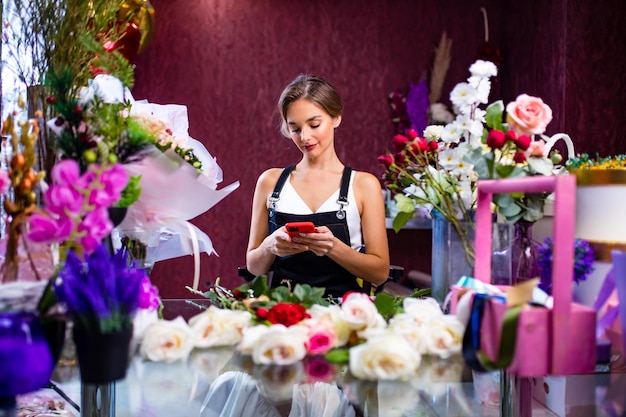 Vrouwelijke bloemist die aan de balie van haar bloemenwinkel staat met haar mobiele telefoon