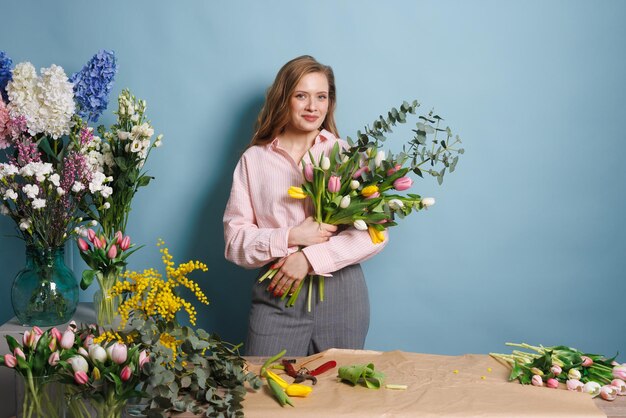 Vrouwelijke bloemist verzamelt een boeket voorjaars tulpenbloemen op een schone blauwe achtergrond