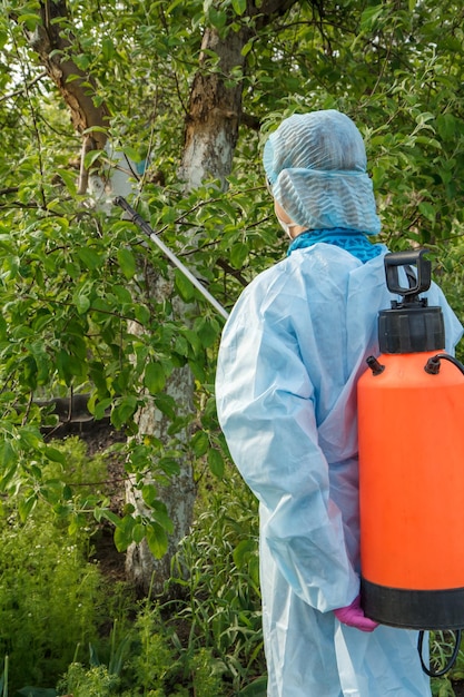 Vrouwelijke boer bespuit appelboom tegen schimmelziekte door chemicaliën met behulp van drukspuit