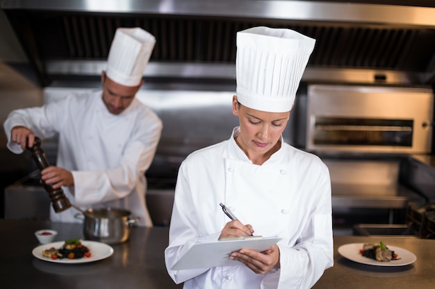 Vrouwelijke chef-kok die op klembord schrijft