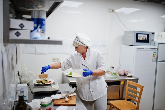 Vrouwelijke chef-kok die salade in Italiaanse restaurantkeuken voorbereidt.