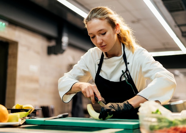 Vrouwelijke chef-kok met handschoen snijdende banaan