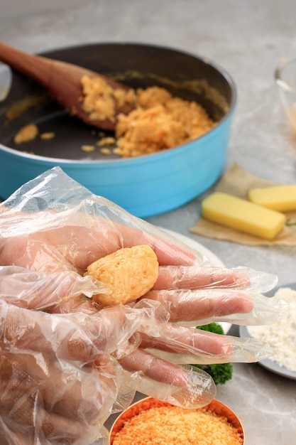 Vrouwelijke chef-kokhand die plastic handschoen gebruikt die Arancini-kaas of rijstnugget of rijstbal gevuld met mozarella gebruikt