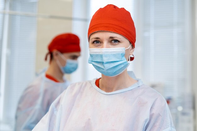 Vrouwelijke chirurg met een beschermkap en masker die met haar collega's op de achtergrond staat en glimlacht. Dokter tijdens operatie. geneeskunde concept