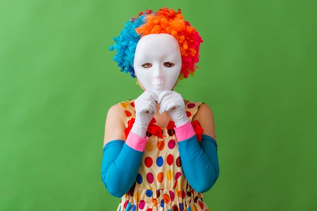 Vrouwelijke clown die in kleurrijke pruik een masker op haar gezicht houdt.