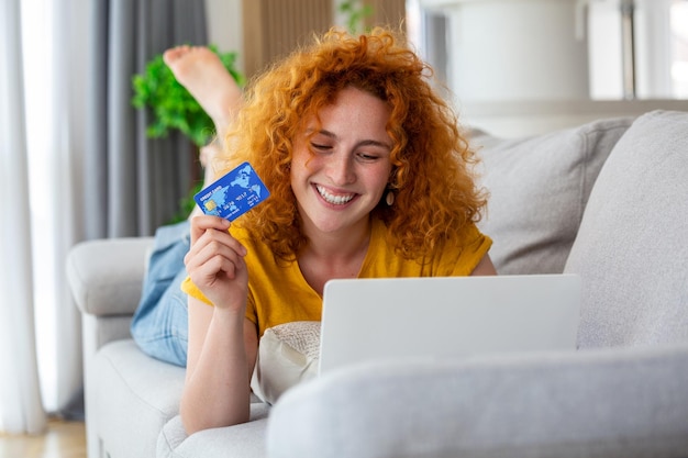 Vrouwelijke consumentenbestedingen kopen op internet levensstijl Gelukkige vrouw online winkelen met laptop thuis Vrouw met behulp van laptopcomputer online winkelen met creditcard spelen online glimlachend binnenshuis