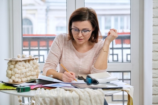 Vrouwelijke decorateur die met materiaalmonsters werkt, stoffen selecteert en modellen van gordijnen tekent