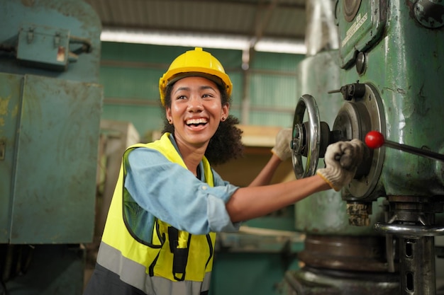 Vrouwelijke fabrieksarbeider in de veiligheidshelm met fabriek voor zware industrie op de achtergrond met verschillende onderdelen van metaalbewerkingsprojecten. Werk in de fabriek voor zware industrie.