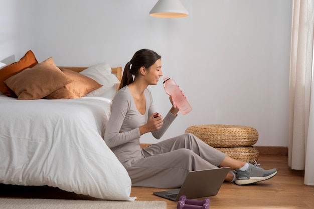 Foto vrouwelijke fitnessinstructeur die thuis gehydrateerd blijft terwijl ze les geeft