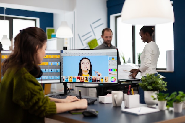 Vrouwelijke fotograaf bewerkt foto's in het kantoor van een creatief mediabureau en retoucheert de klant met een styluspotlood op de computer