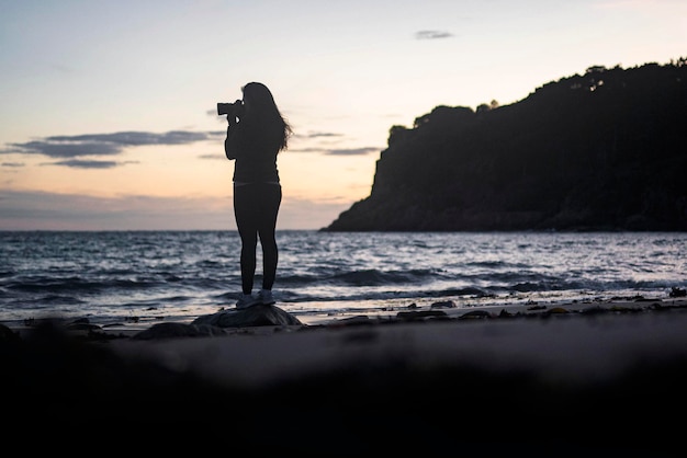 Vrouwelijke fotograaf die de zonsondergang vastlegt bij Portelet Bay, Isle of Jersey