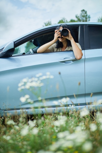 Foto vrouwelijke fotograaf zit in de auto en fotografeert een landschap met bloemenvelden, reisvrouw neemt foto, ruimte voor tekst.