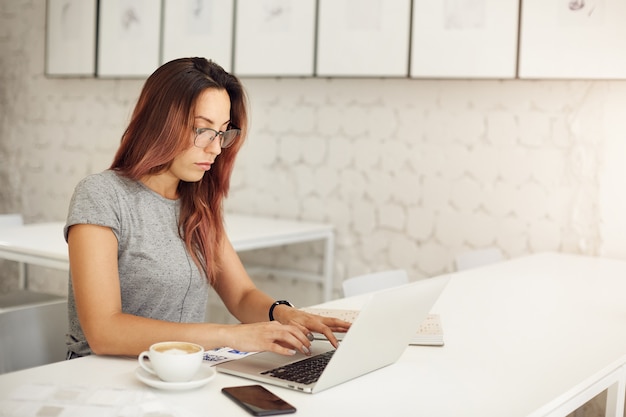 Vrouwelijke freelance scenarioschrijver die laptop gebruikt om haar nieuwe meesterwerk in een café weg van huis te creëren om haar creatieve blok te bestrijden.