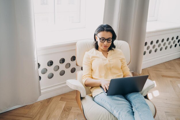 Vrouwelijke freelance werknemer werkt bij laptop zittend in een fauteuil op kantoor aan huis Verre baan concept