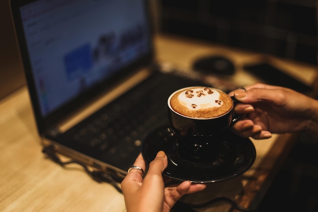 Vrouwelijke freelancer die online op de computer werkt terwijl hij een koffiemok met latte art vasthoudt. concept van netwerken