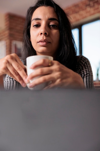 Vrouwelijke freelancer die op afstand werkt op laptop, bedrijfsrapport doet met netwerkapp thuis op computer. Werken aan onderzoeksinformatie over opstarten en online studeren, klasles.