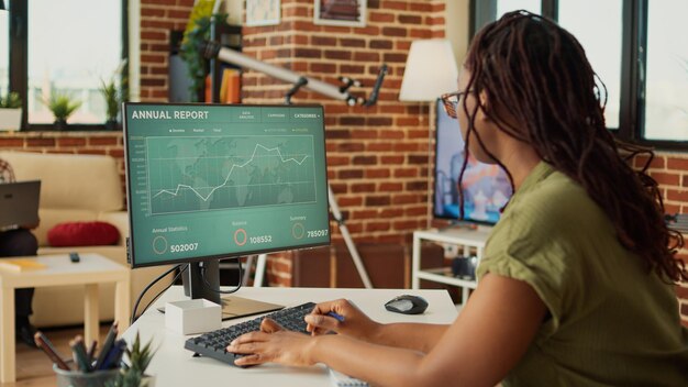 Vrouwelijke freelancer kijkt naar het jaarlijkse verkooprapport op de computer en analyseert boekhoudkundige gegevensstatistieken op het web. Vrouw die op afstand werkt met financiële diagrammen, marketingonderwijs thuis.