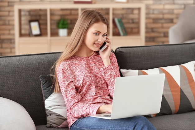 Vrouwelijke freelancer praten via de telefoon tijdens het werken op laptop thuis