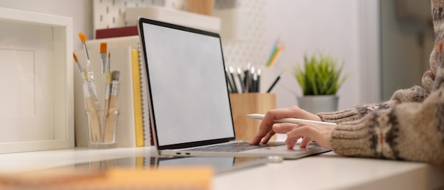 Vrouwelijke freelancer typen op mock-up laptop op moderne werkruimte met tekengereedschappen en benodigdheden