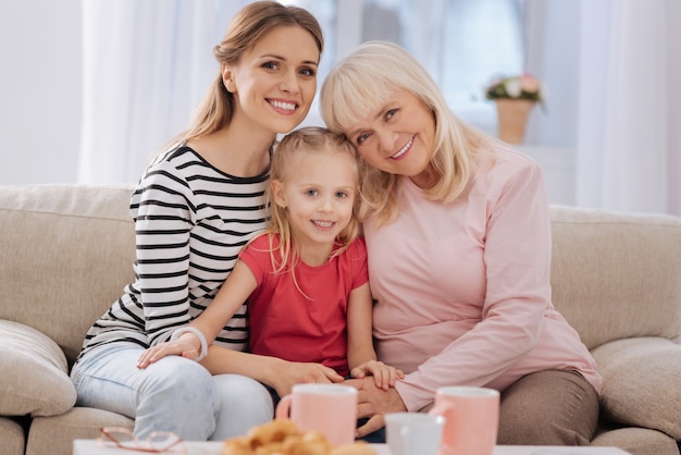 Vrouwelijke generaties. Leuke gelukkige vrolijke familie die bij elkaar zit en naar je kijkt terwijl je thuis bent