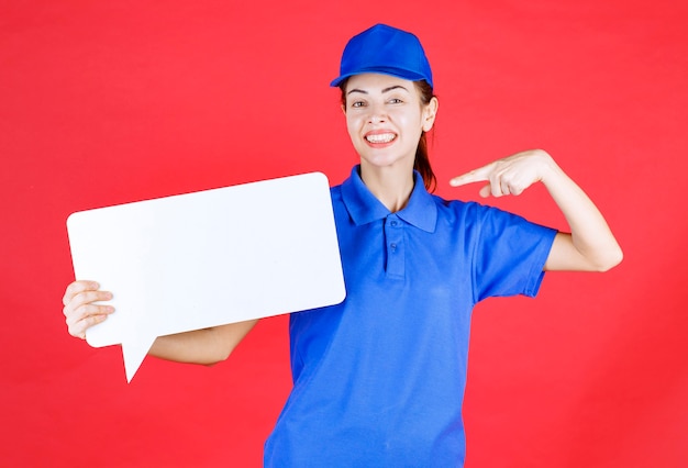 Vrouwelijke gids in blauw uniform met een wit rechthoekig infobord.