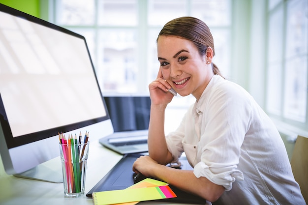 Vrouwelijke grafisch ontwerper praten over telefoon aan balie