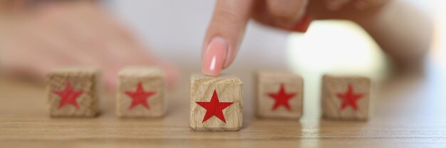 Vrouwelijke hand bewegende houten kubus met sterrensymbool op tafel die feedback, reactie en beoordeling geeft