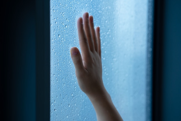 Vrouwelijke hand bij het raam tijdens de regen. Glas in druppels water.