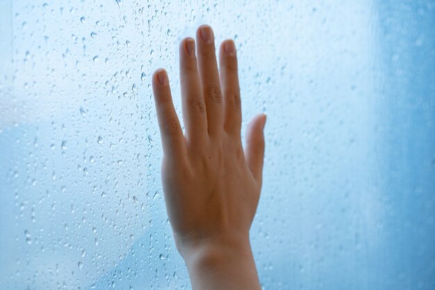 Vrouwelijke hand bij het raam tijdens de regen. glas in druppels water.