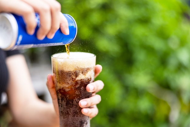 Vrouwelijke hand die cola van blik naar glas giet