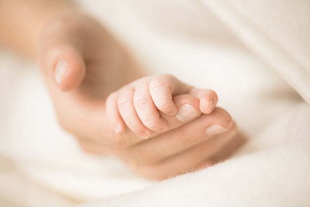Vrouwelijke hand die de hand van haar pasgeboren baby houdt. Mam met haar kind. Zwangerschap, familie, geboorte concept.