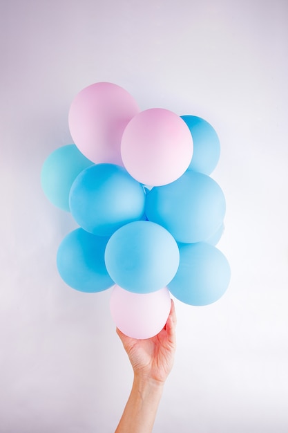 Vrouwelijke hand die een reeks kleine roze en blauwe baloons lika houdt een wolk op witte achtergrond