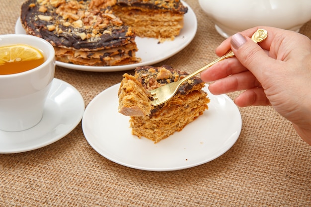 Vrouwelijke hand die een vork vasthoudt en zelfgemaakte chocoladetaart gaat proeven, liggend op een witte schotel met een zak op de achtergrond.