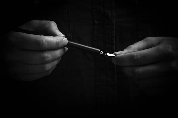 Vrouwelijke hand die elegant een inktpen vasthoudt met een metalen punt close-up op een zwarte achtergrond klassieke vulpen geïsoleerde macro zwart-wit kopie ruimte